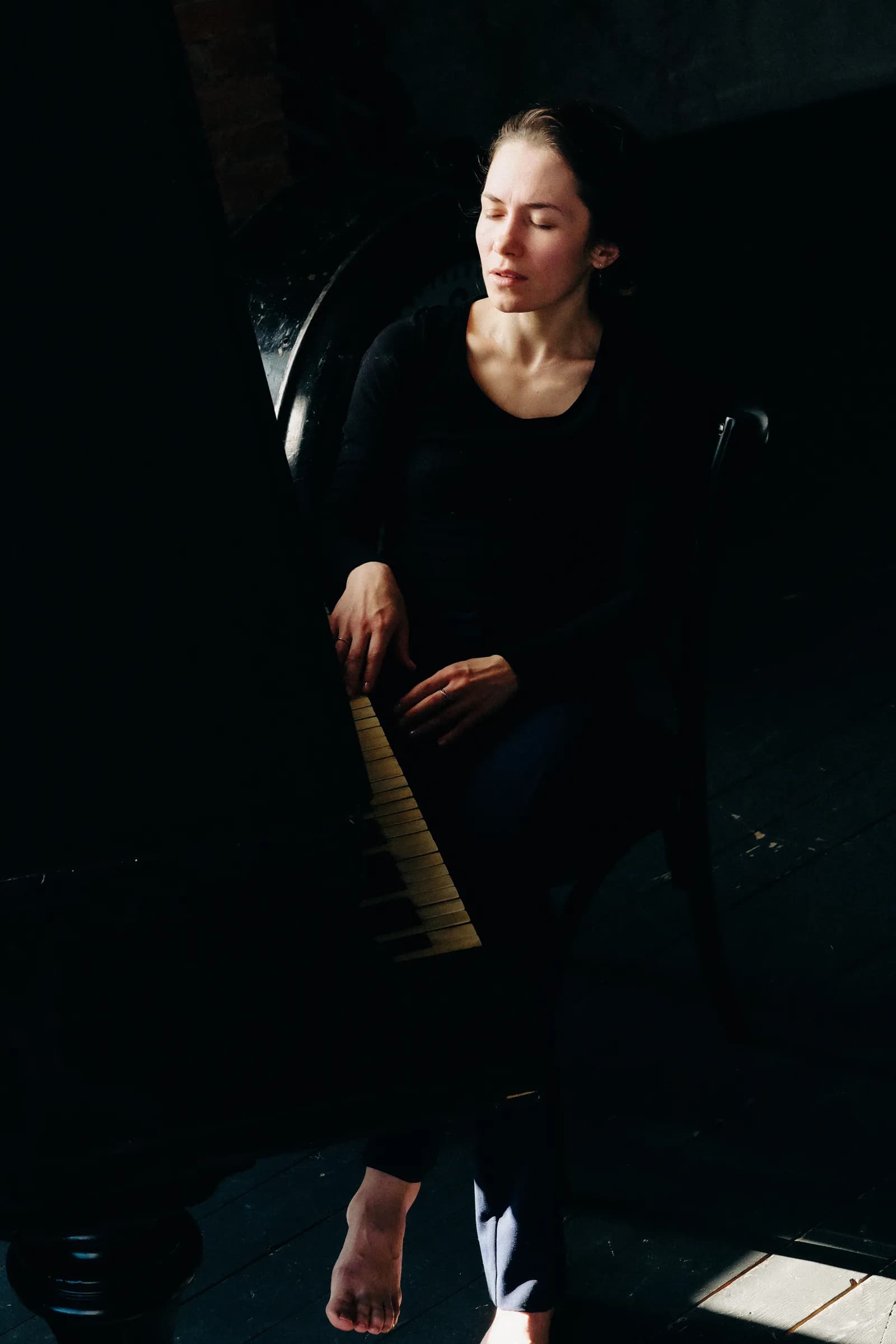 Woman seen from above, one hand resting along the piano keyboard, eyes closed