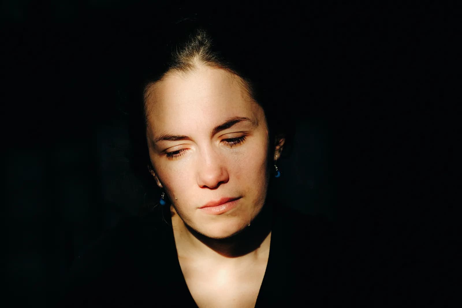 Close portrait of a woman with lowered eyes, a band of sun across her face in the dark