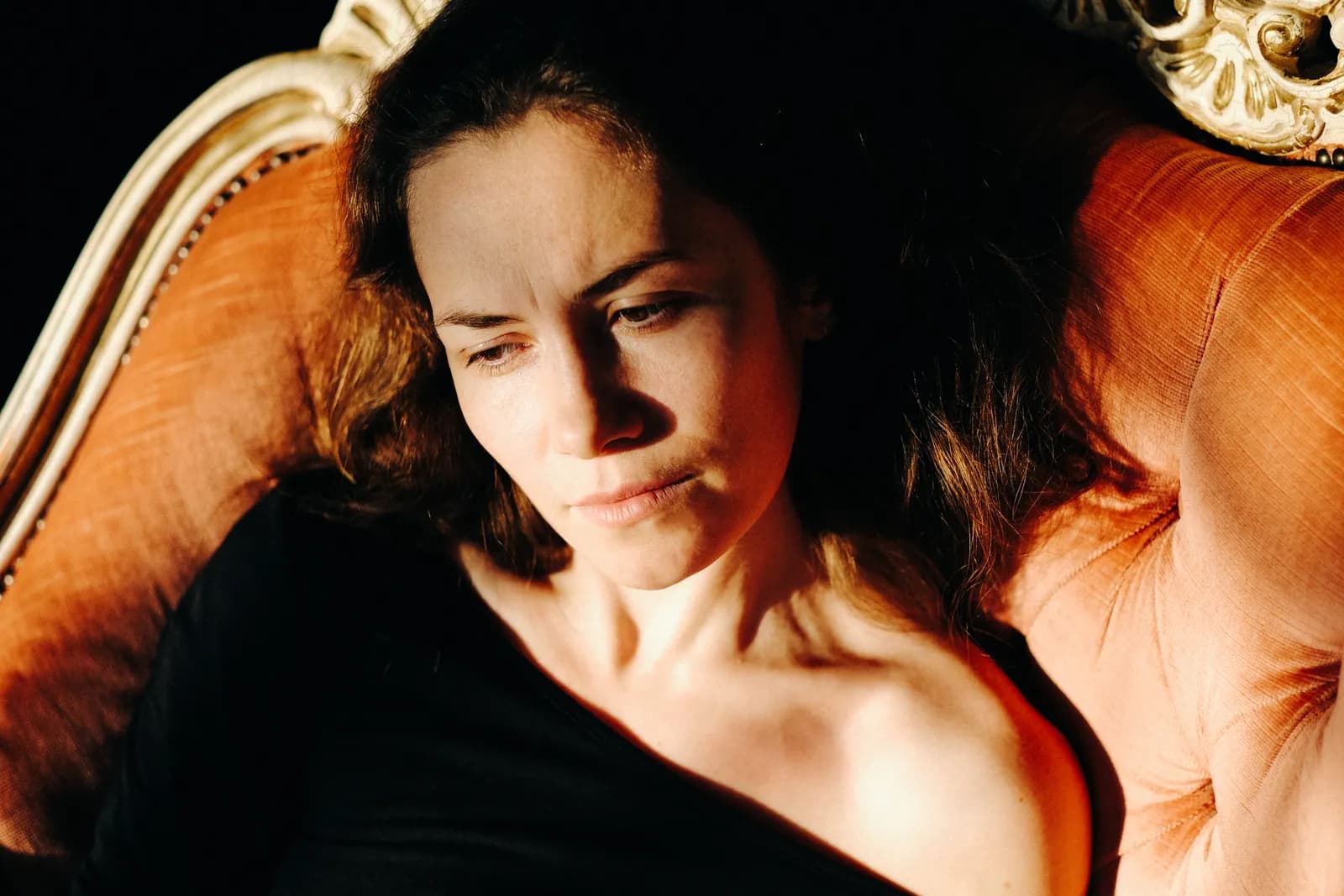 Close portrait of a woman resting against the back of an orange baroque armchair, sunlit