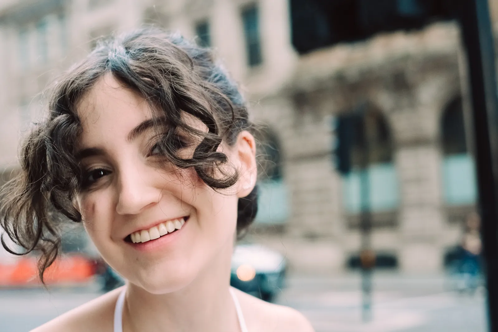 Close portrait of a smiling woman with dark curls on a City street, traffic blurred behind