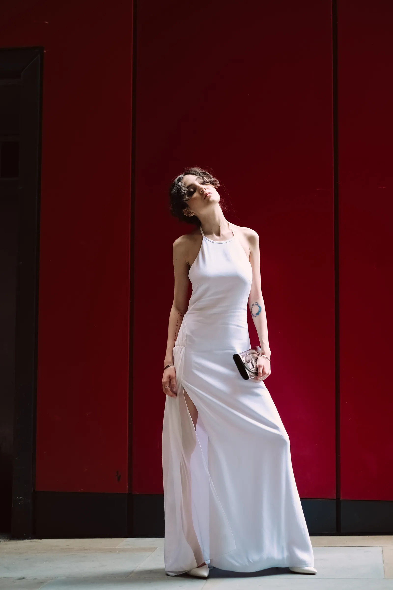 Woman in a white gown against a deep red wall, head thrown back