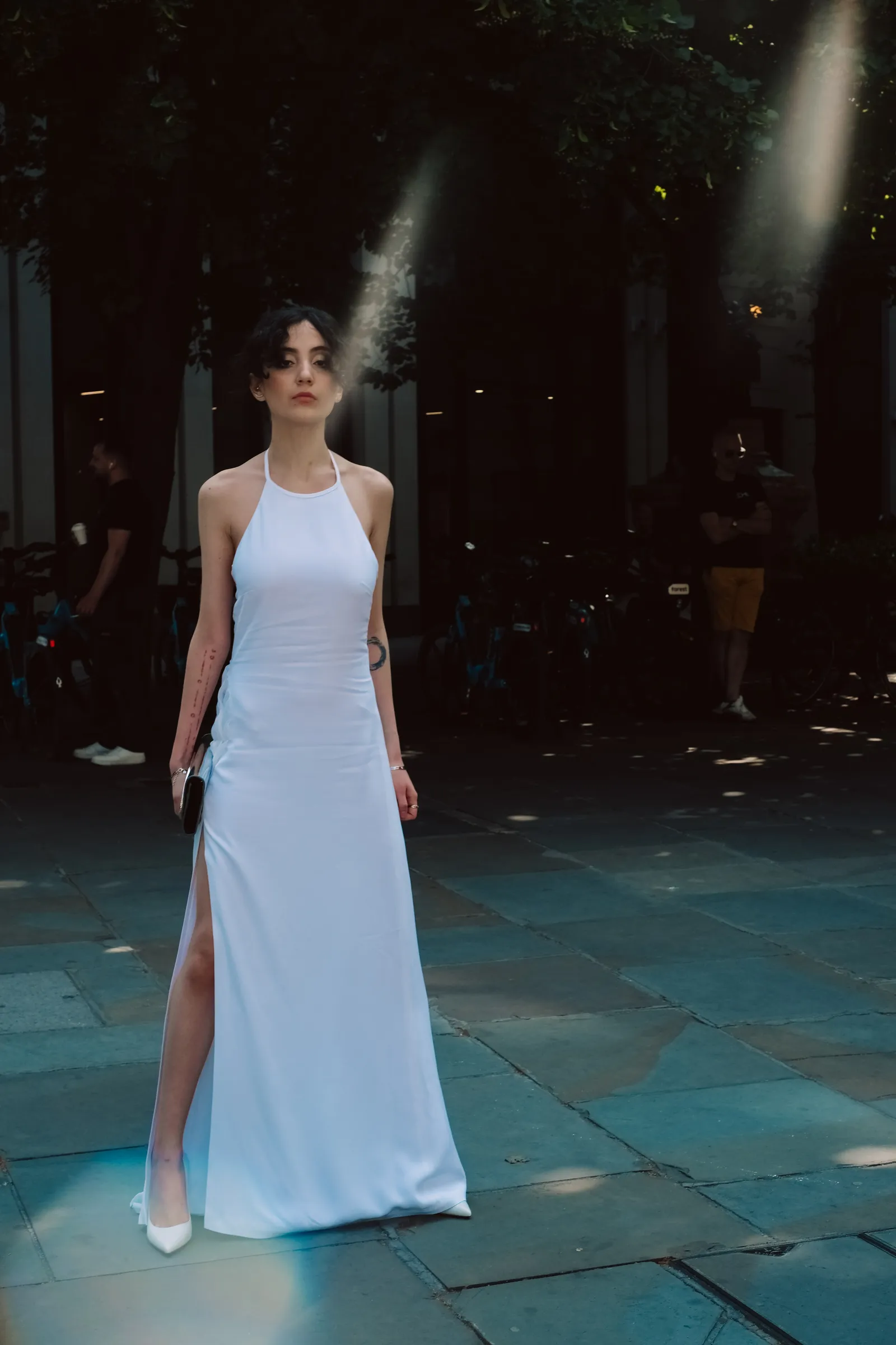 Woman in a white gown exhaling smoke in a dark City courtyard