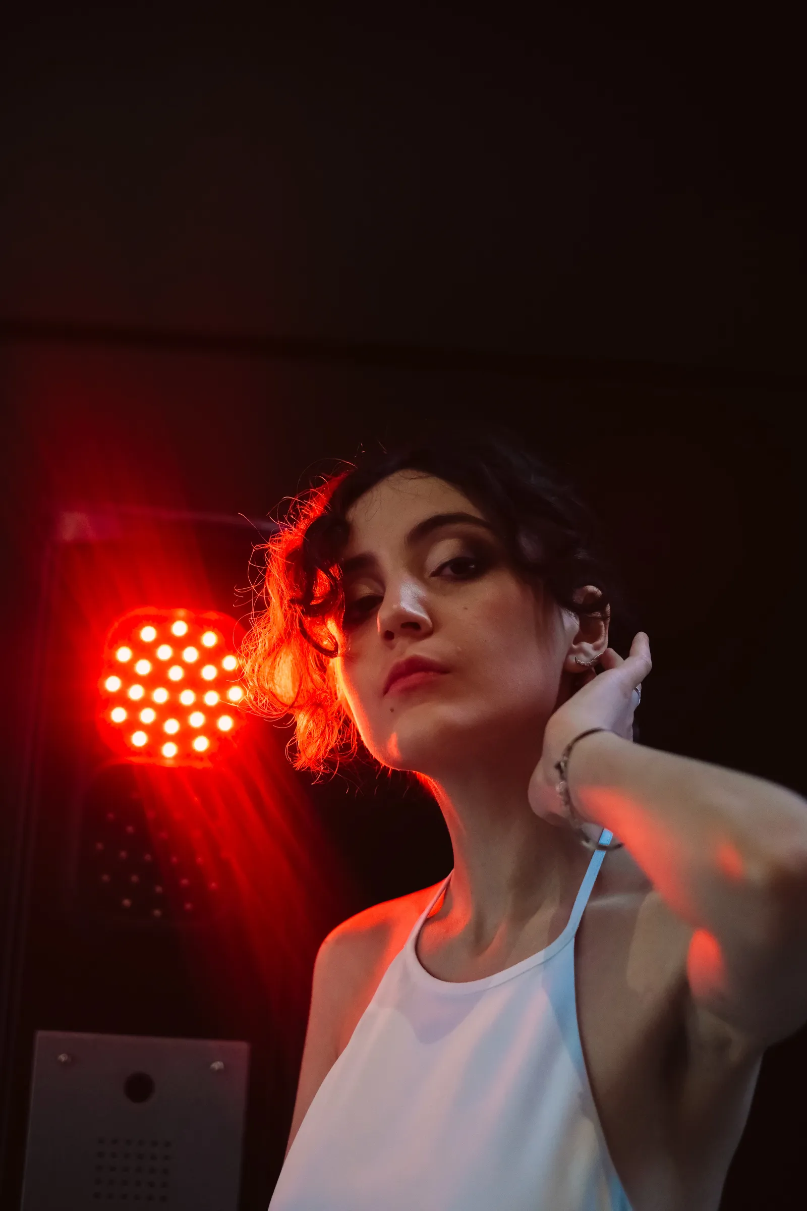 Woman glancing down past a glowing red stage lamp, bare shoulders in white