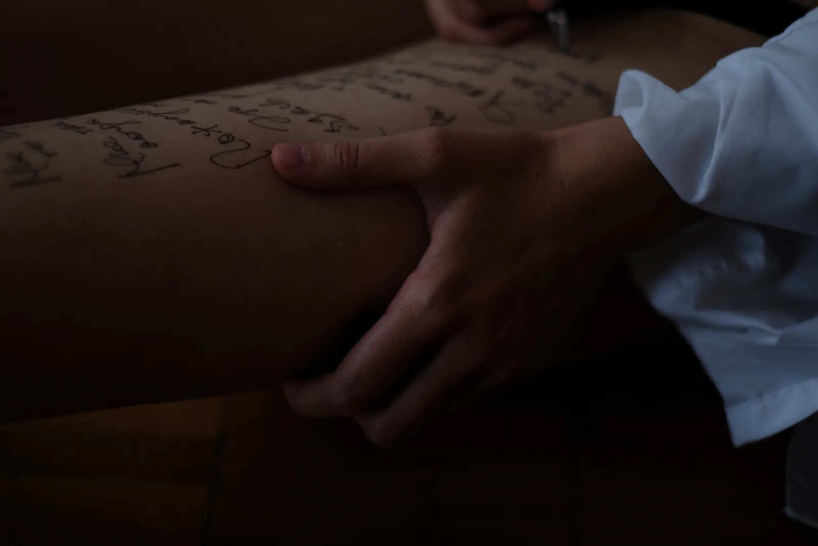 Hand gripping a thigh covered in lines of handwriting