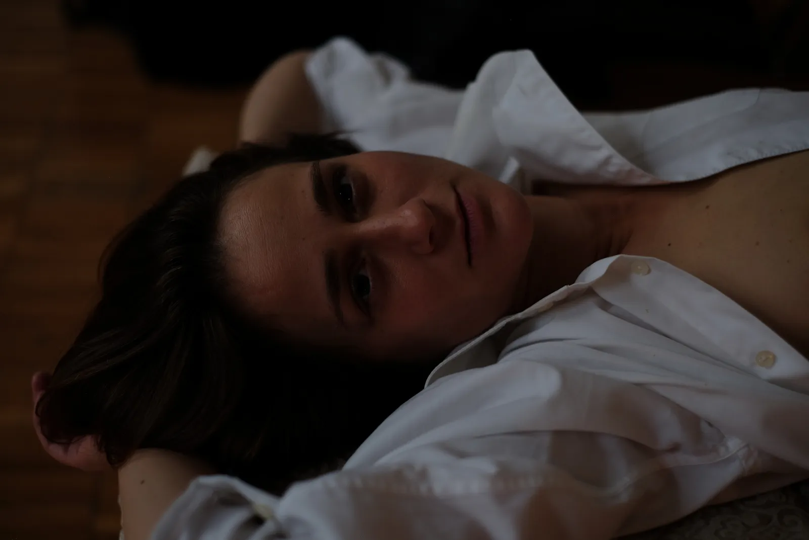Woman in a white shirt lying on her back, looking straight into the lens