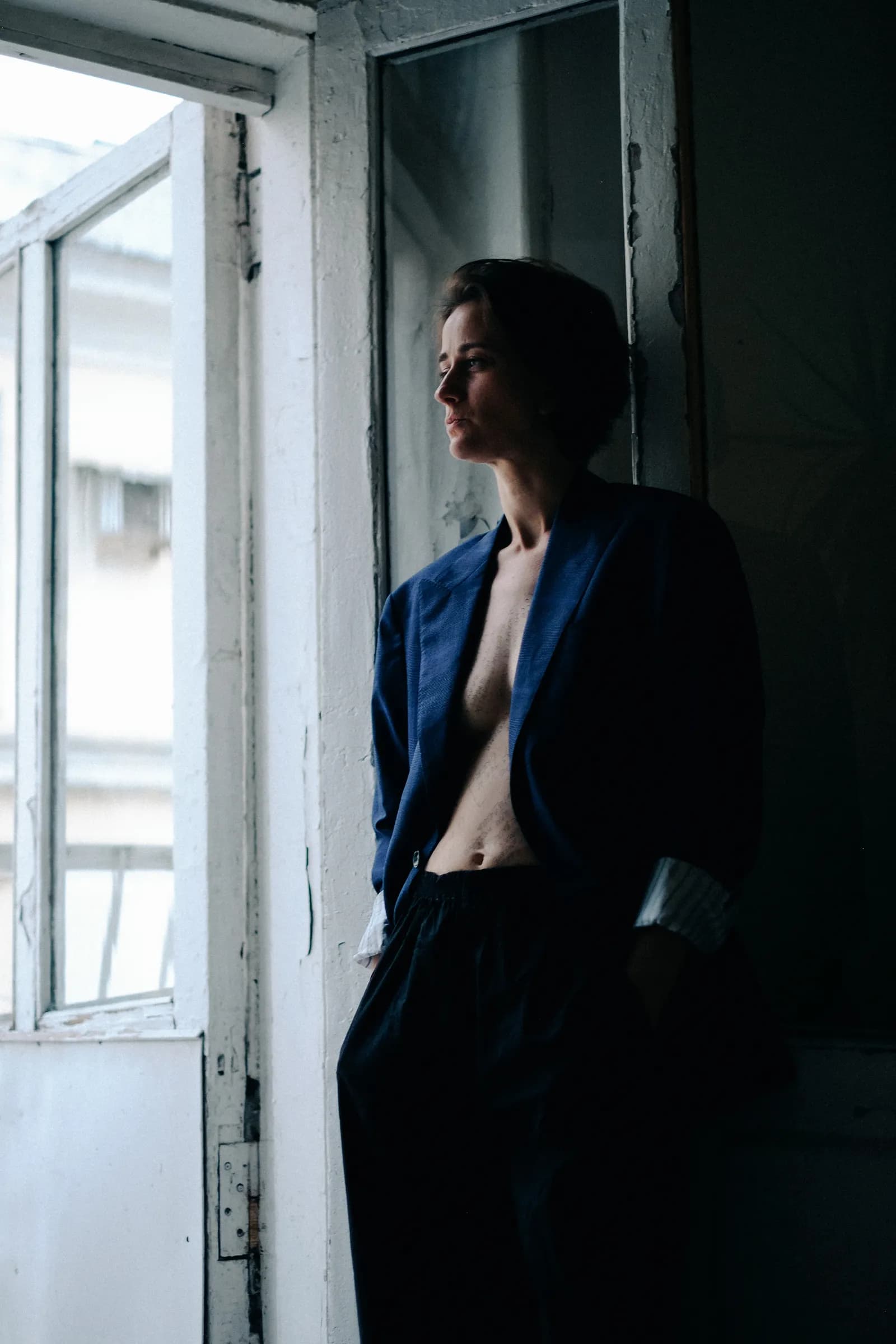 Woman in a loose navy suit standing in a tall balcony doorway, looking out