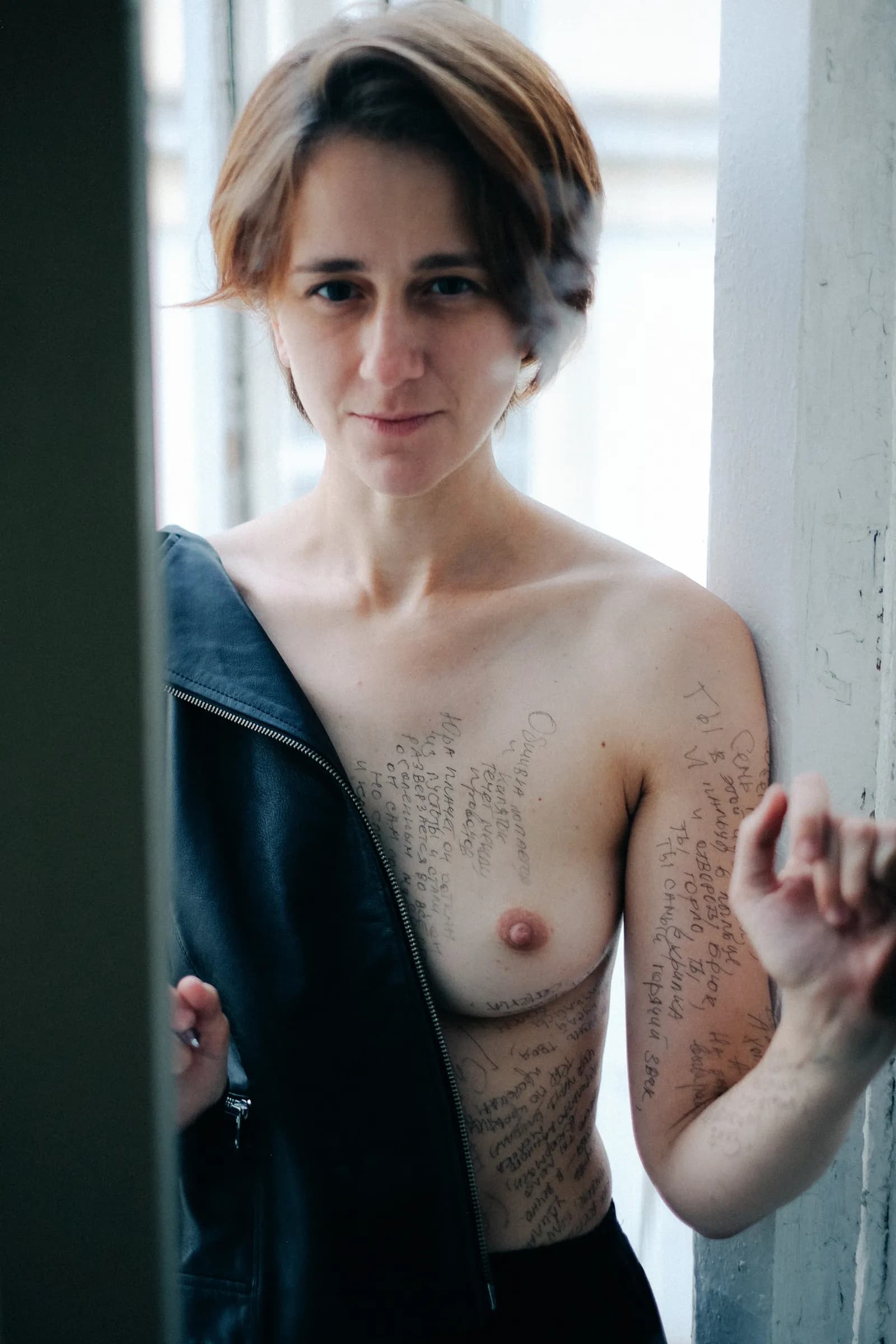Woman with a leather jacket slipping from her shoulder looking into the lens, chest covered in handwriting
